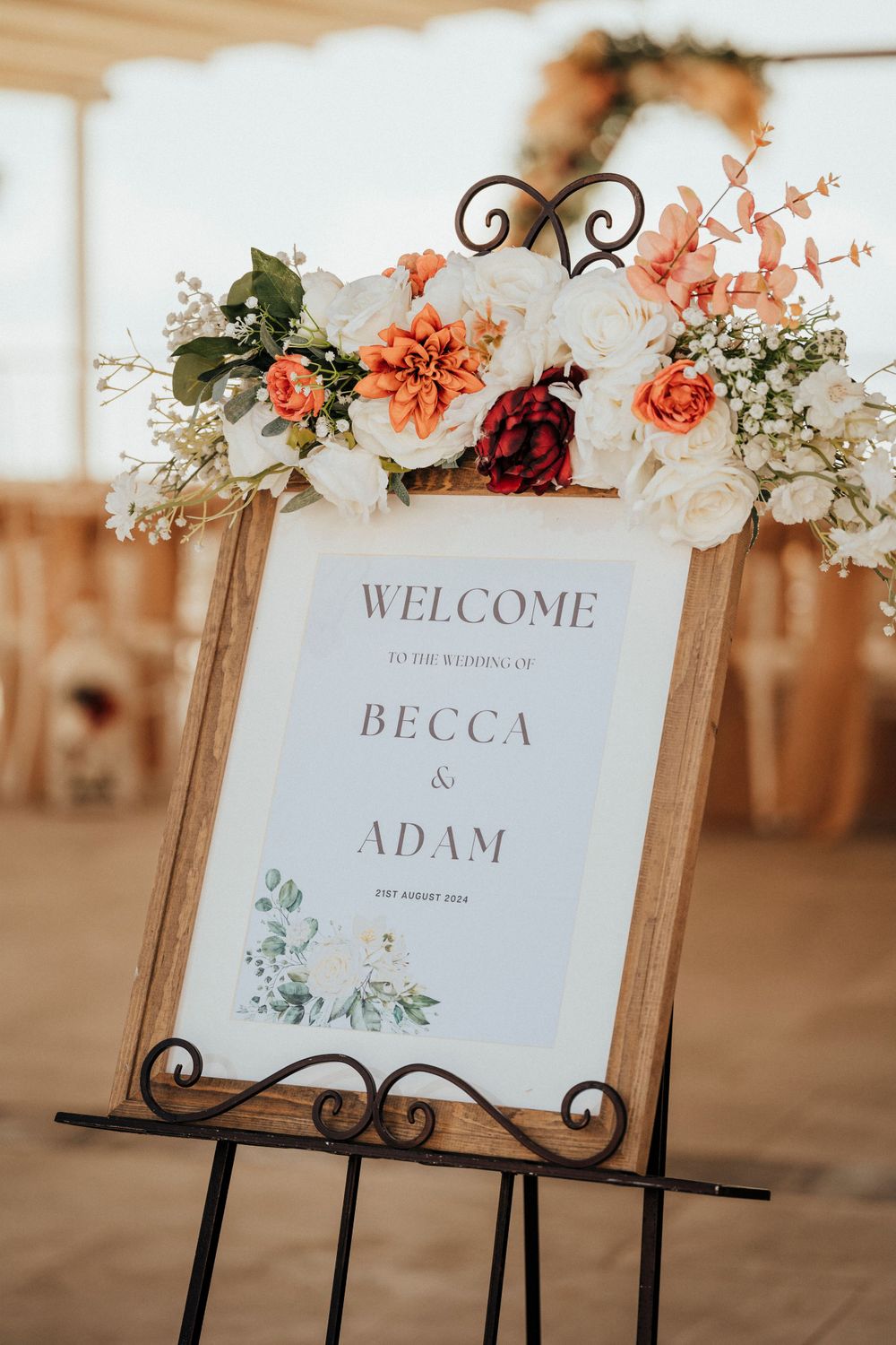 A wedding welcome sign decorated with coral and white flowers in an ornate frame.