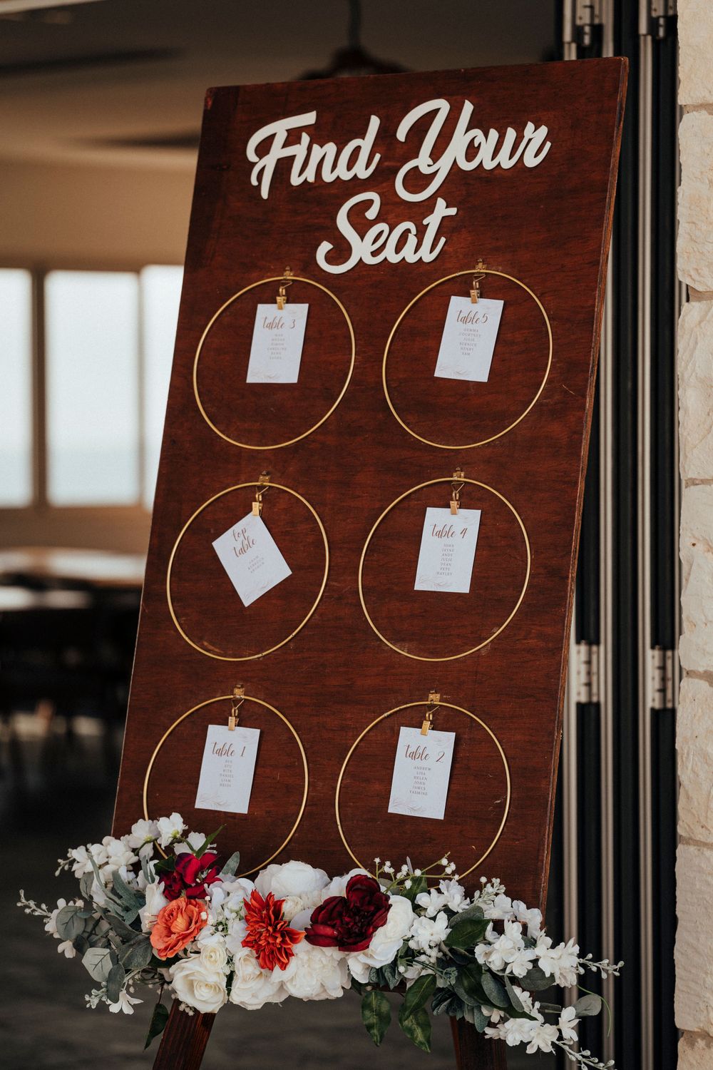 Rustic wooden wedding seating chart board with white and red floral decorations at the base.