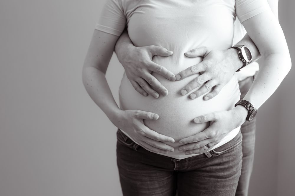 Black and white photograph of hands cradling a pregnant belly in a tender moment.