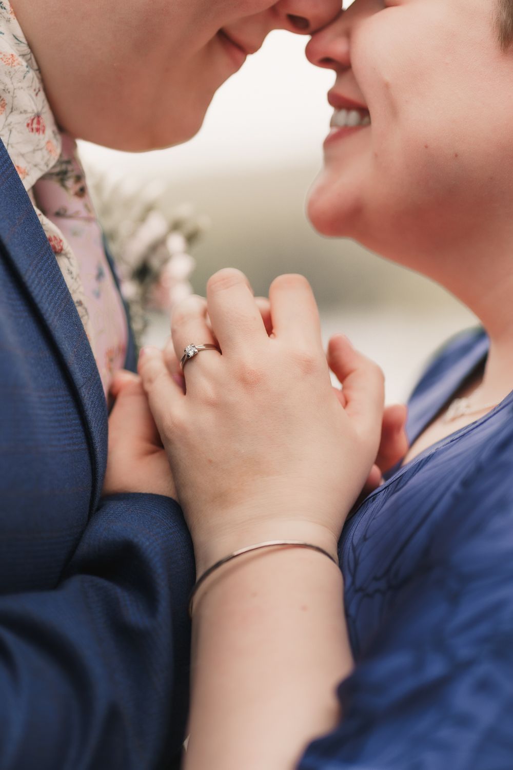 Close-up shot of two people's clasped hands with engagement ring and bracelet visible as they share an intimate moment.
