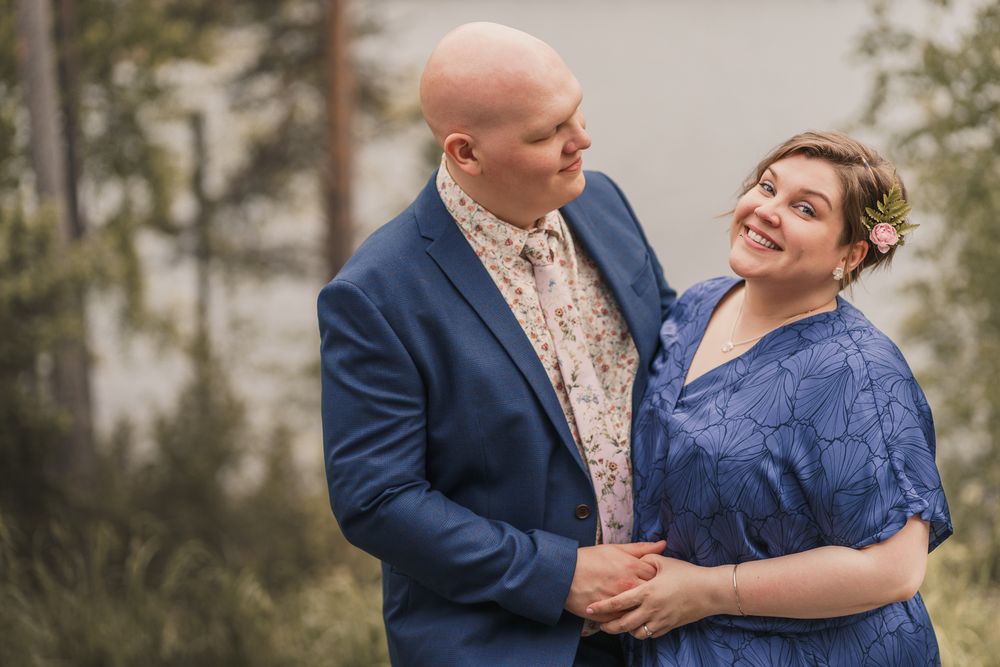 A couple in wedding attire share romantic moments outdoors with the groom in a navy suit and bride wearing a yellow flowered crown.
