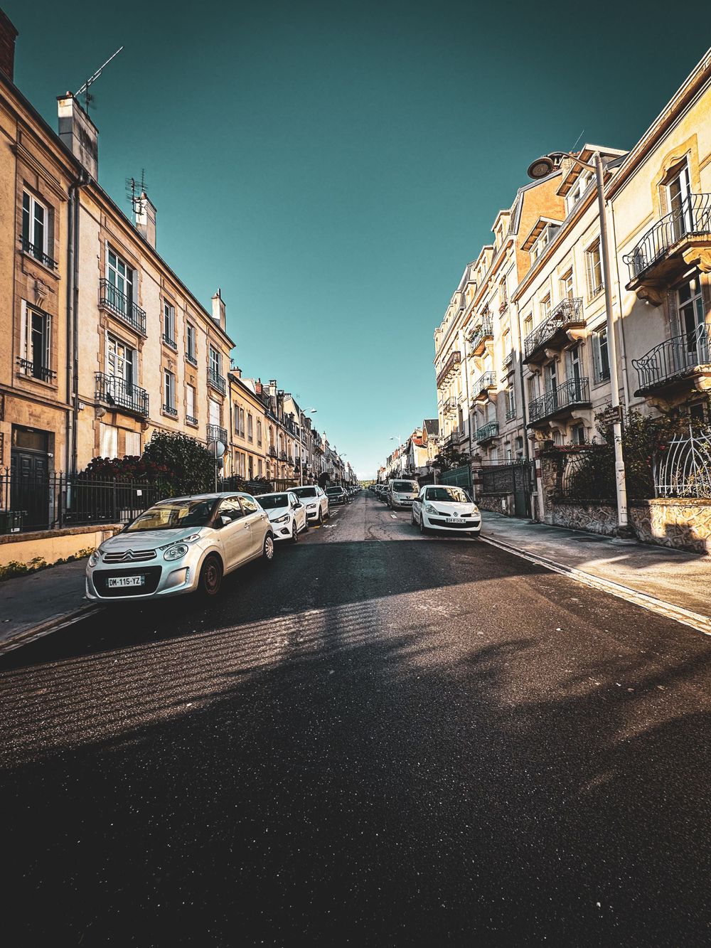 Symmetrical urban street lined with classic architecture and parked cars under teal sky.