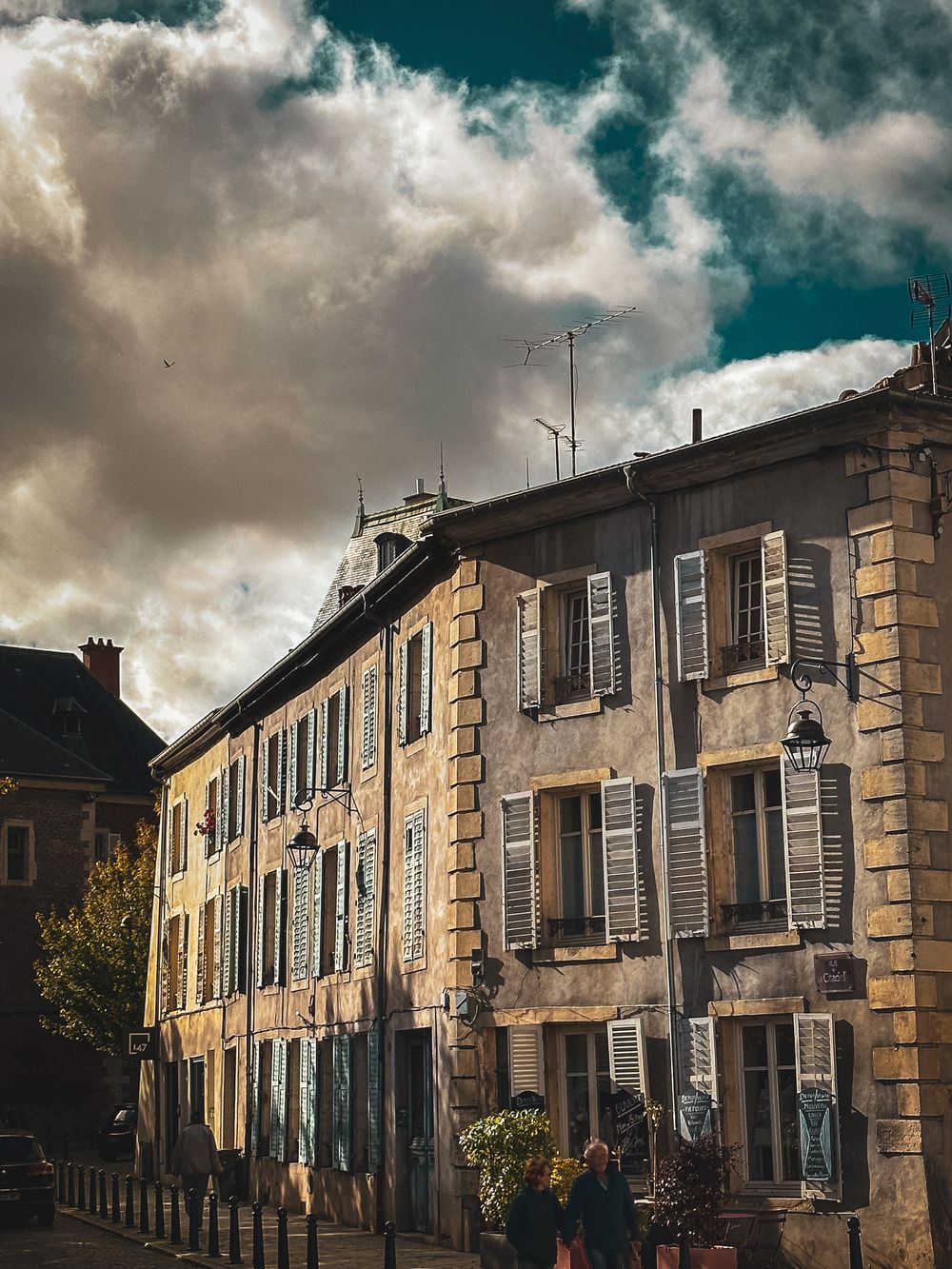 Historic European building facade with blue shutters and ornate stonework under dramatic cloudy skies.