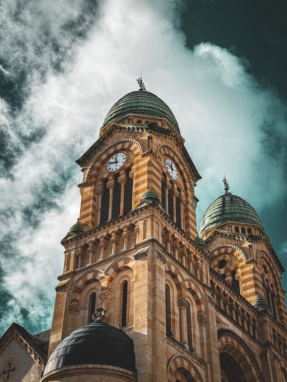 Majestic cathedral towers with copper domes against a turquoise sky with wispy clouds.