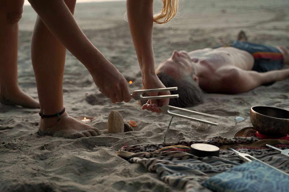 Healing tools and equipment arranged on a beach blanket at sunset.