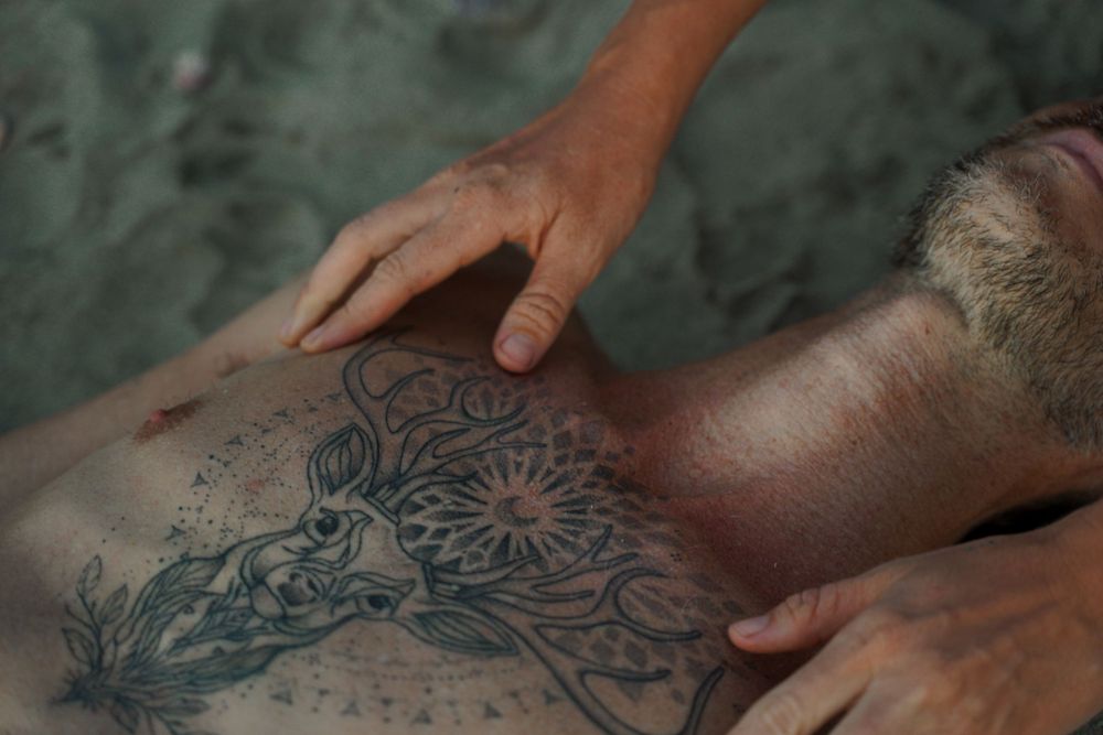 Close up of hands performing massage on tattooed skin.