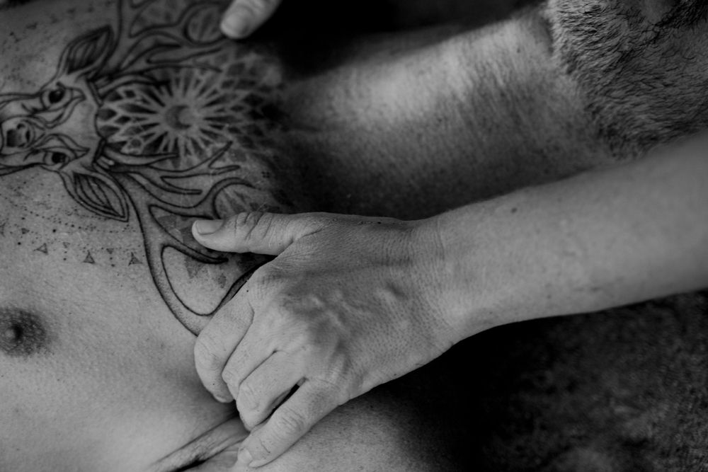 Black and white image of hands massaging near ornate tattoo design.