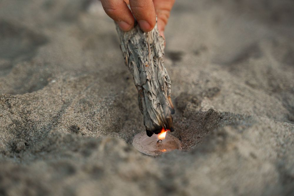 Hand placing smoking sage or incense into beach sand.