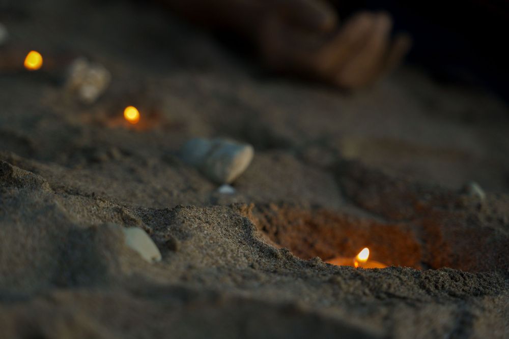 Small candles glowing in the sand at dusk creating peaceful ambiance.
