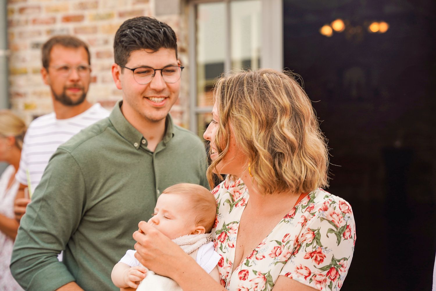 Family group standing together outdoors against brick wall.