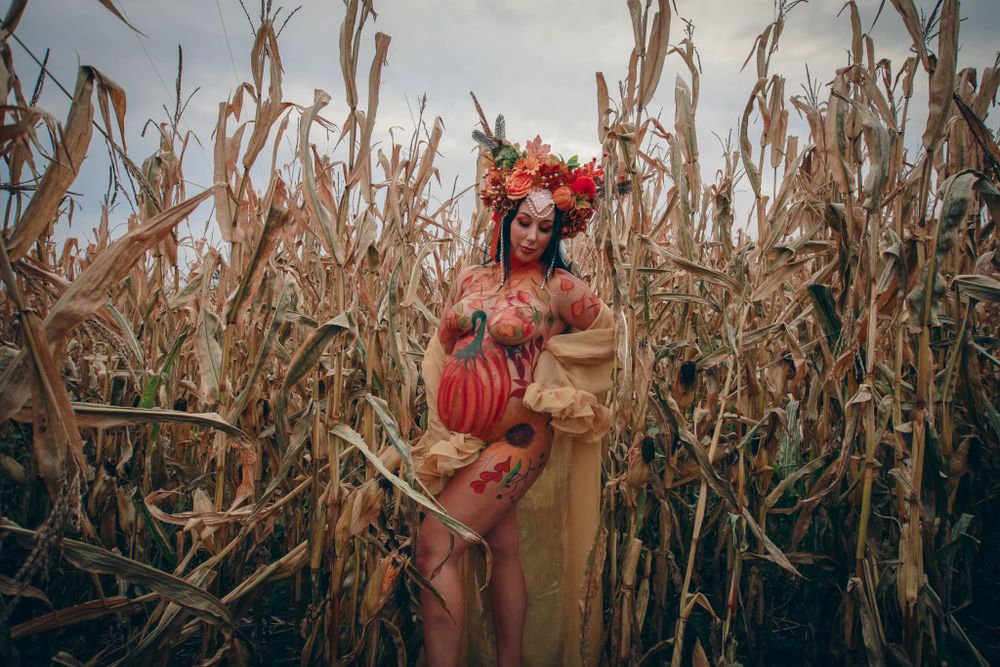 Artistic maternity portrait in dried corn field with autumn-themed costume and styling.