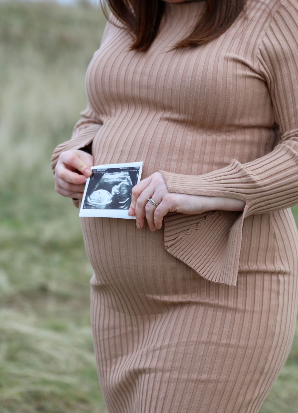 Pregnant woman in ribbed dress holds ultrasound photo against her growing belly.