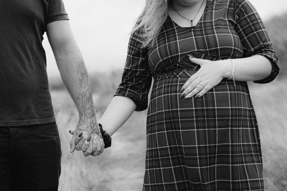 Black and white close-up of couple holding hands with pregnant belly in plaid dress.