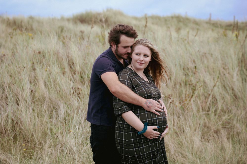 Intimate maternity photo in golden grass field shows couple embracing baby bump.