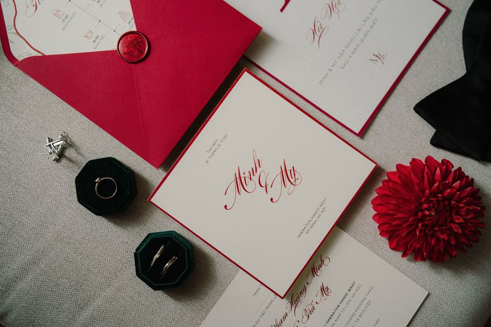 Elegant wedding invitation suite in red and white with floral accents and calligraphy displayed on marble background.