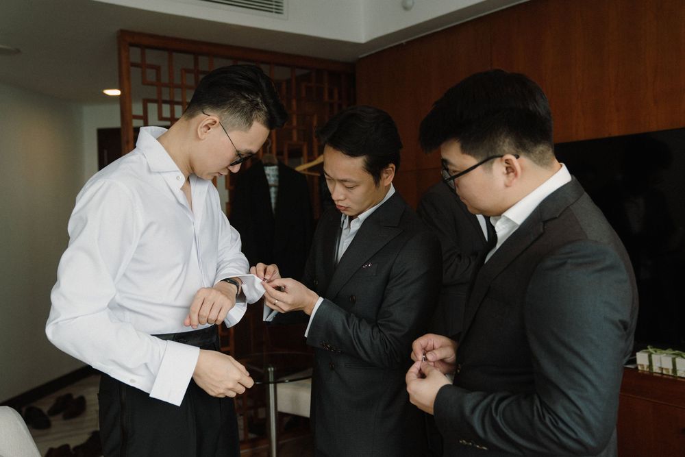 Business professionals in formal attire huddle together to light cigarettes in an office setting.