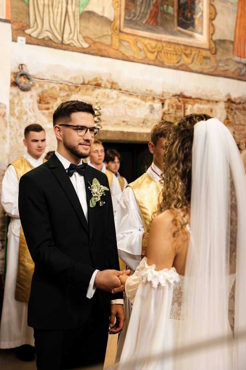 Pan młody wpatrzony w Panią młodą w trakcie przysięgi małżeńskiej
