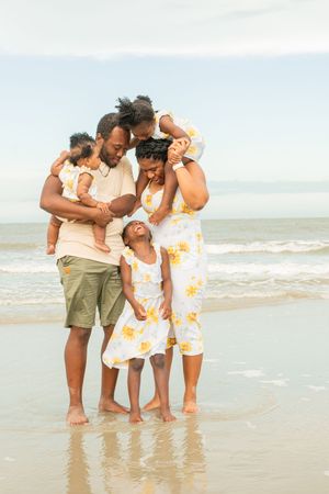 A loving family shares a joyful moment together on the beach at sunset with waves and sand in the background.