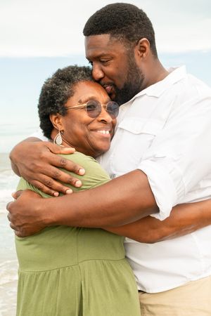 A loving couple embraces on the beach, sharing a tender moment while wearing casual summer attire.