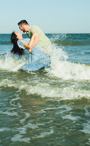 A couple dances together in the ocean waves at sunset, creating a romantic and playful moment by the sea.