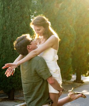 A romantic couple embraces while dancing outdoors at sunset with golden sunlight filtering through the trees.