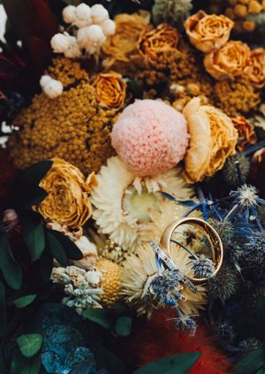 Dried floral arrangement in warm golden tones with white blooms and delicate blue accents against a dark background.