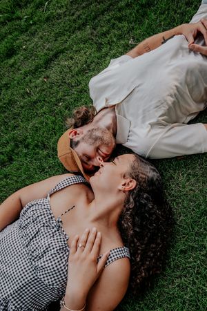 A couple lying together on green grass, with one person wearing a checkered pattern top and another in light clothing.