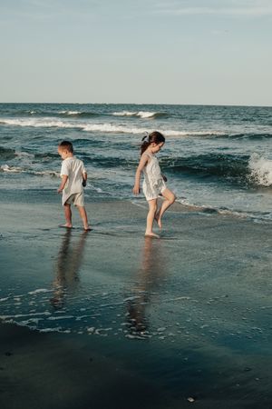 Two children in light colored outfits playing in the waves at the beach on a sunny afternoon.