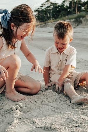 Parent and child playing together in the sand at a beach creating sand castles and formations on a sunny day.
