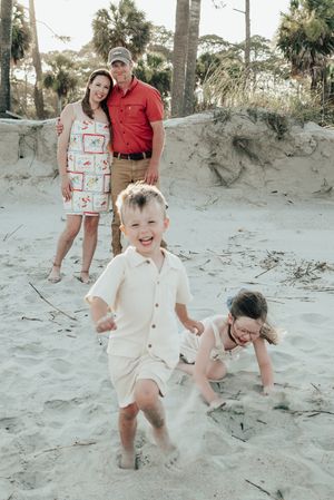 Casual family photoshoot at a sandy beach showing playful moments as kids jump and create movement in the sand.