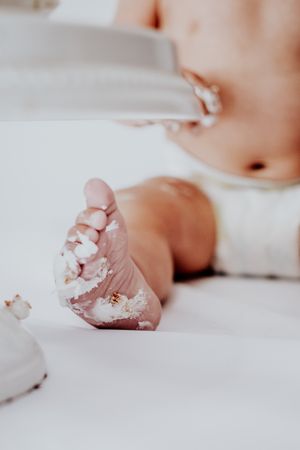 Close up photograph of tiny baby foot covered in white powder against soft white fabric background.