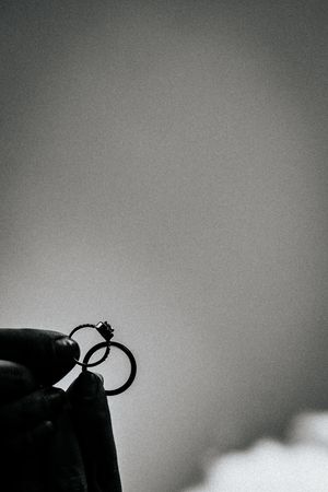 Black and white silhouette of a ring being held against a grey gradient background.