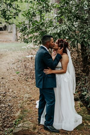 Newlyweds share an intimate kiss on a tree-lined path during their outdoor wedding photoshoot.