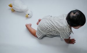 Baby in striped onesie crawling on white surface with toy ducks nearby.