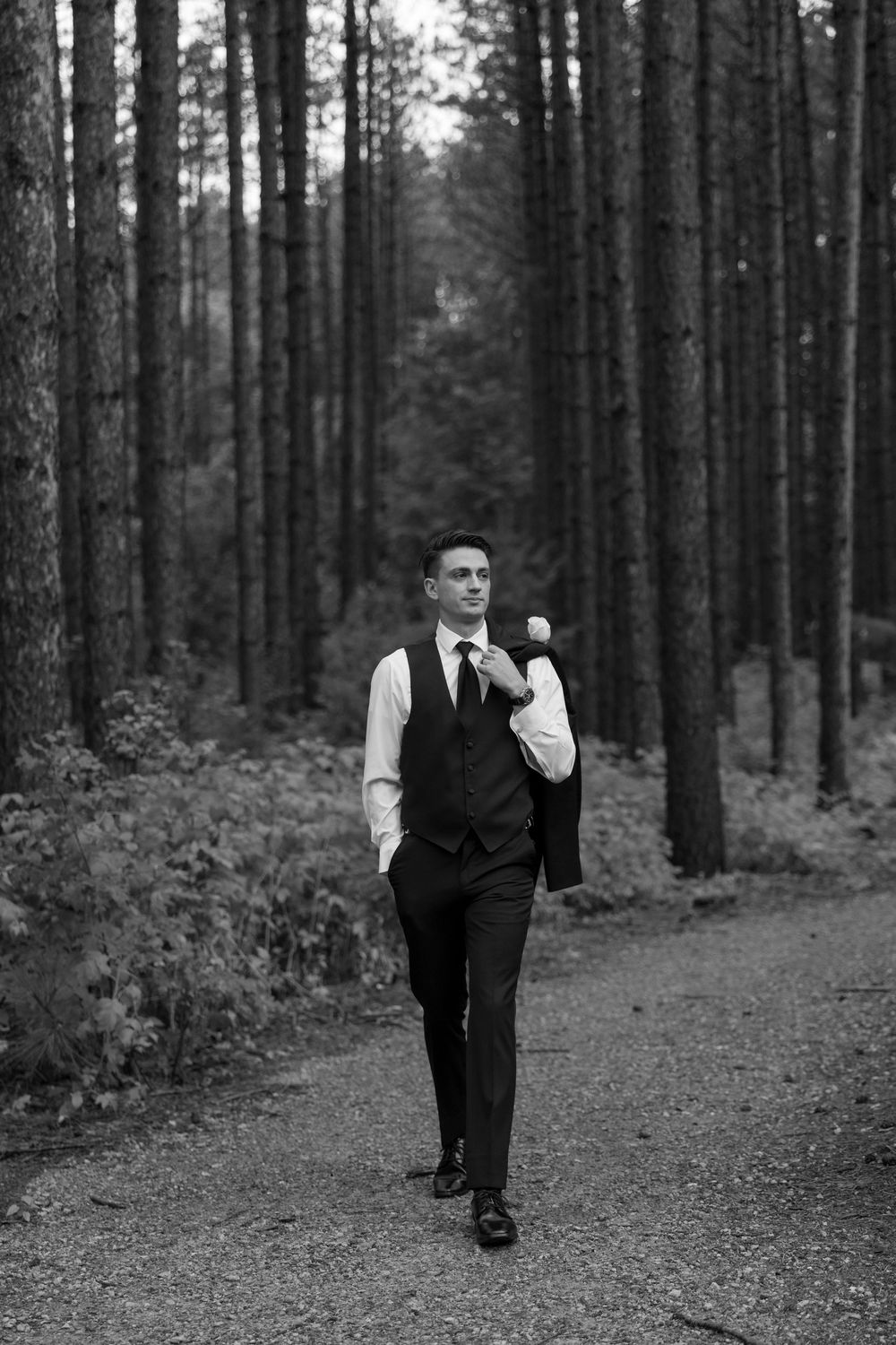 A figure playfully balancing on one leg while walking down a path through a pine forest.