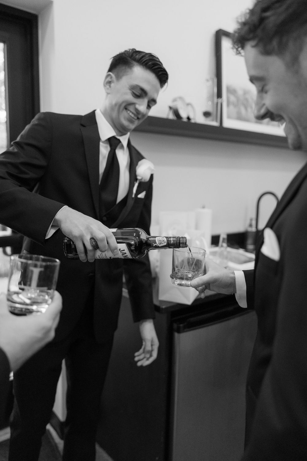 A person in a suit pours drinks during what appears to be a wedding celebration in black and white.