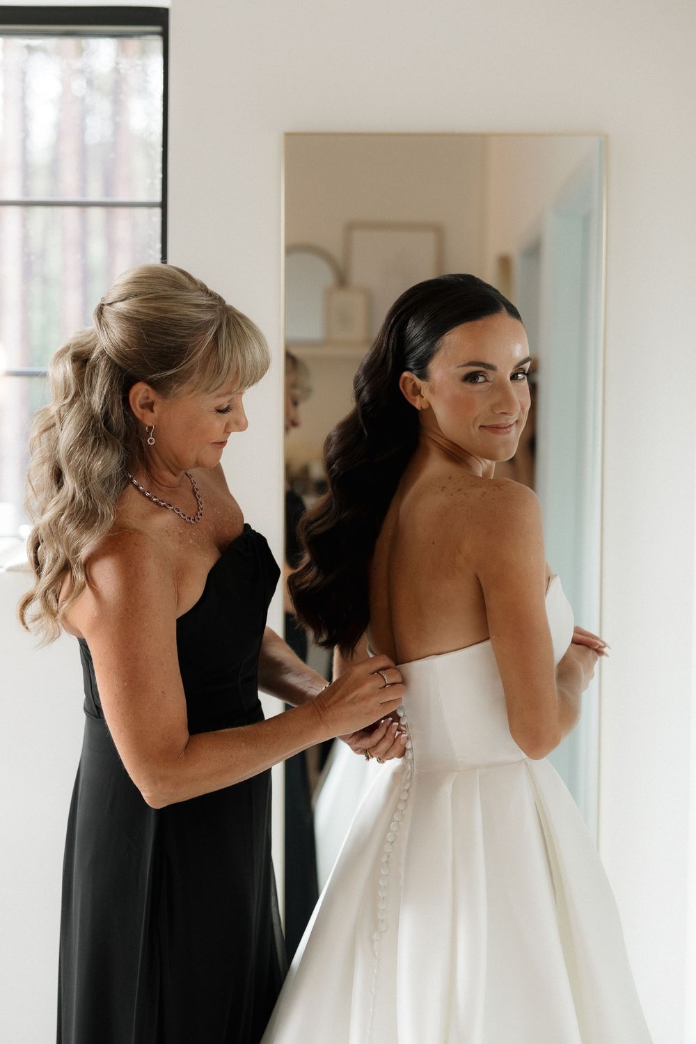 A tender moment during wedding dress preparations in natural window light.