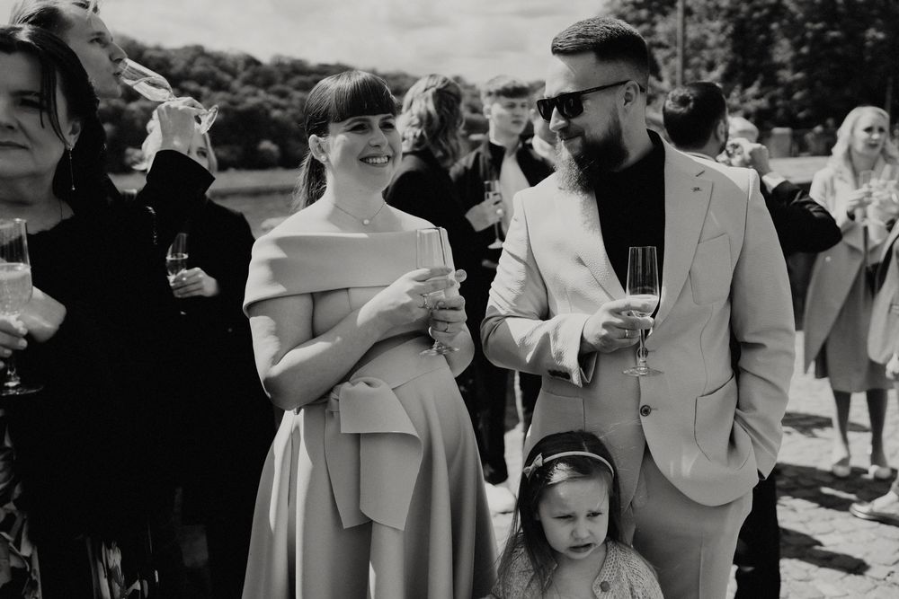 Wedding guests gather outdoors in formal attire during a black and white reception shot.