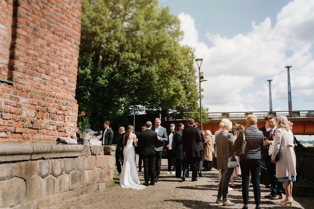 Wedding celebration with guests gathered along brick walls under blue skies.