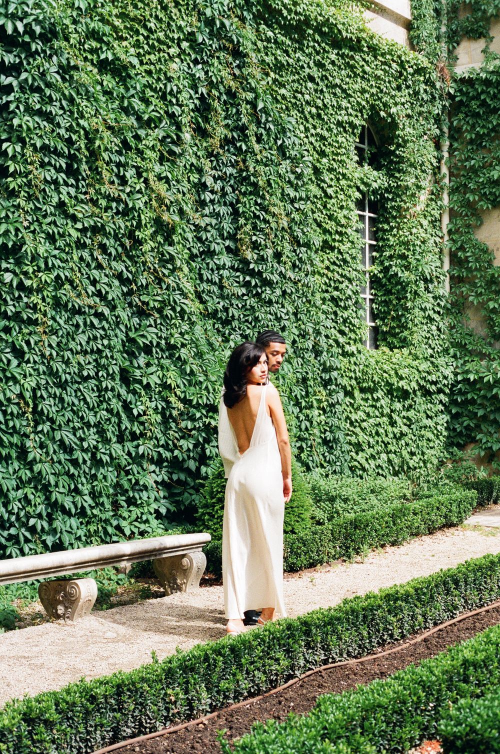 Four sequential photos showing a person in a white dress walking along a path beside an ivy-covered garden wall.