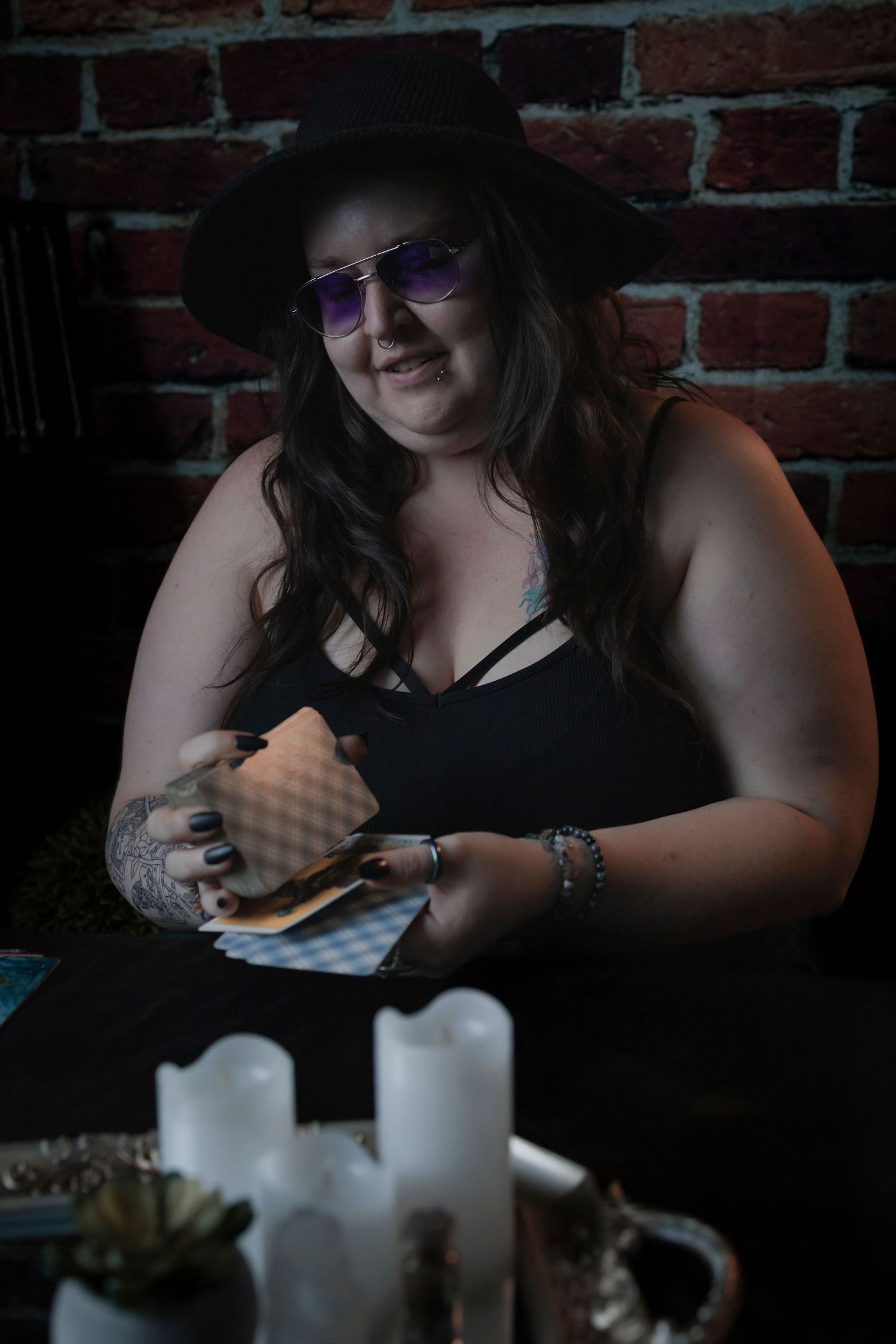 A person in a black top uses a smartphone at a dimly lit table with white candles and a brick wall backdrop.