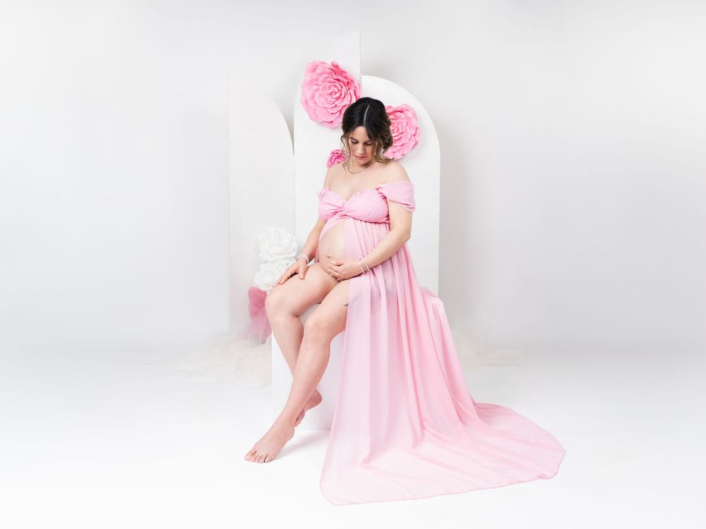 Maternity photo session with flowing pink dress against white backdrop.
