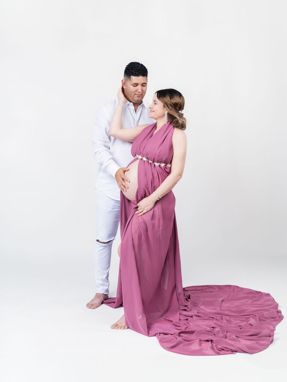 A romantic maternity session with a flowing mauve dress on a white backdrop.