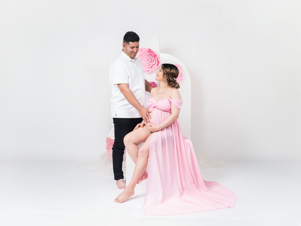 Intimate maternity photo session with pink dress and white background.