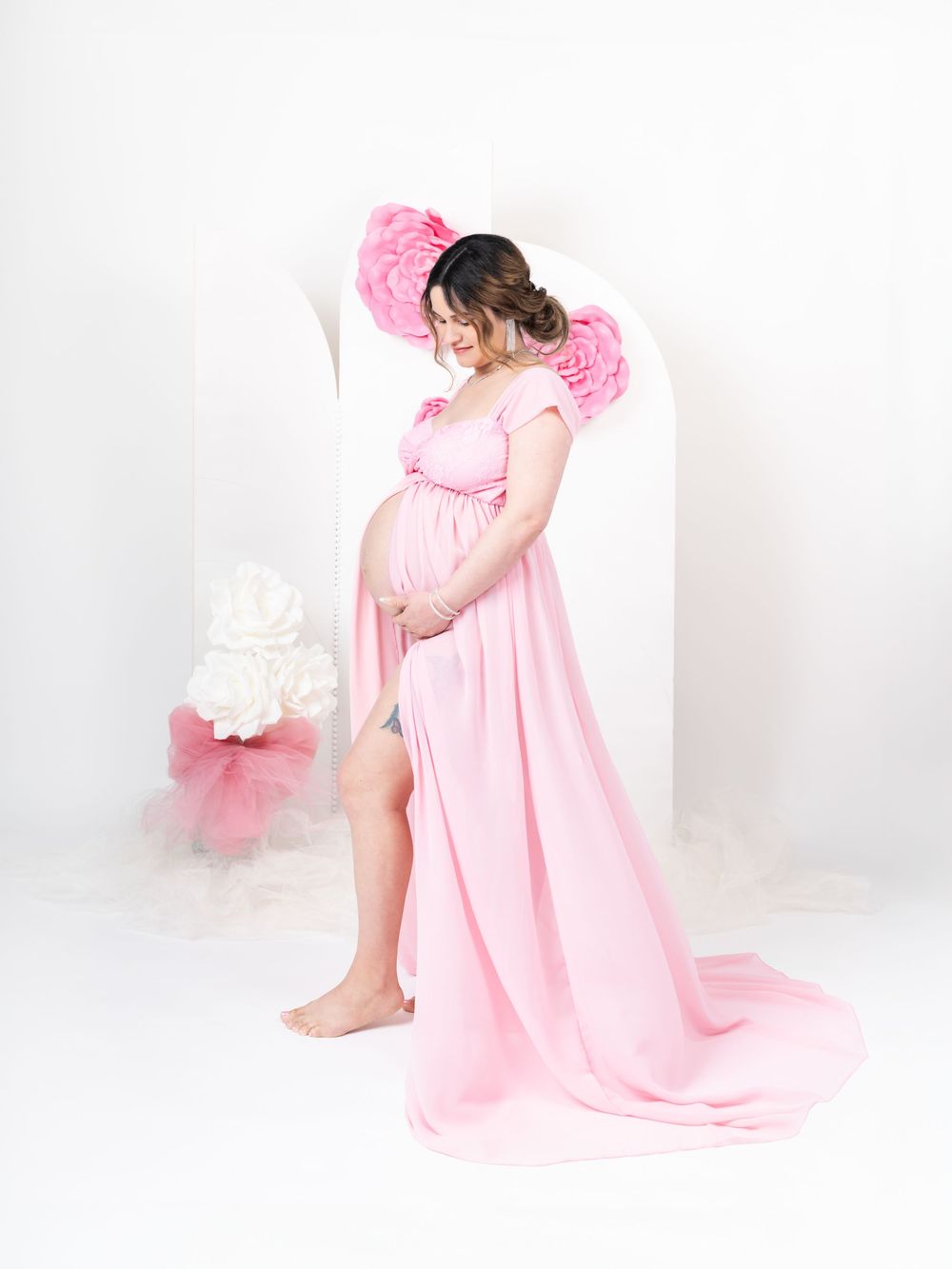Romantic maternity portraits in soft pink flowing gown against white backdrop.