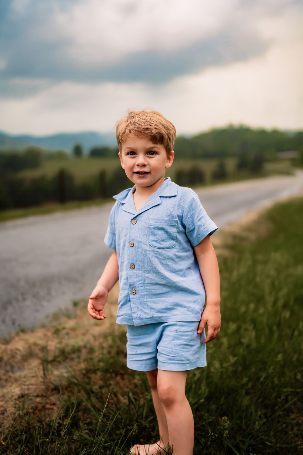 Toddler in light blue matching set playing outdoors on a cloudy day with mountains in the background.