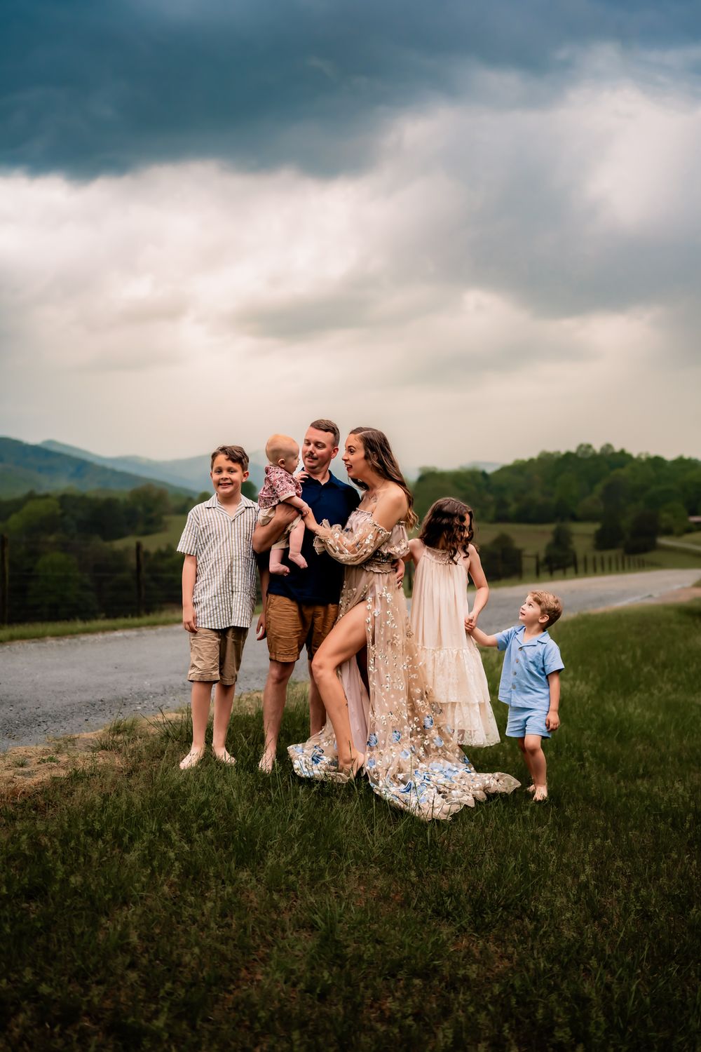Family enjoying a playful moment together in a grassy field with mountains and cloudy skies as backdrop.