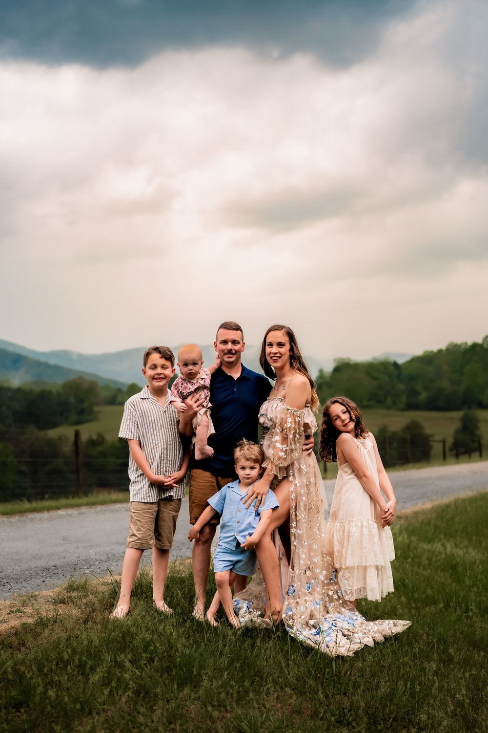A happy group poses on a hillside with mountains and a winding road in the distance.