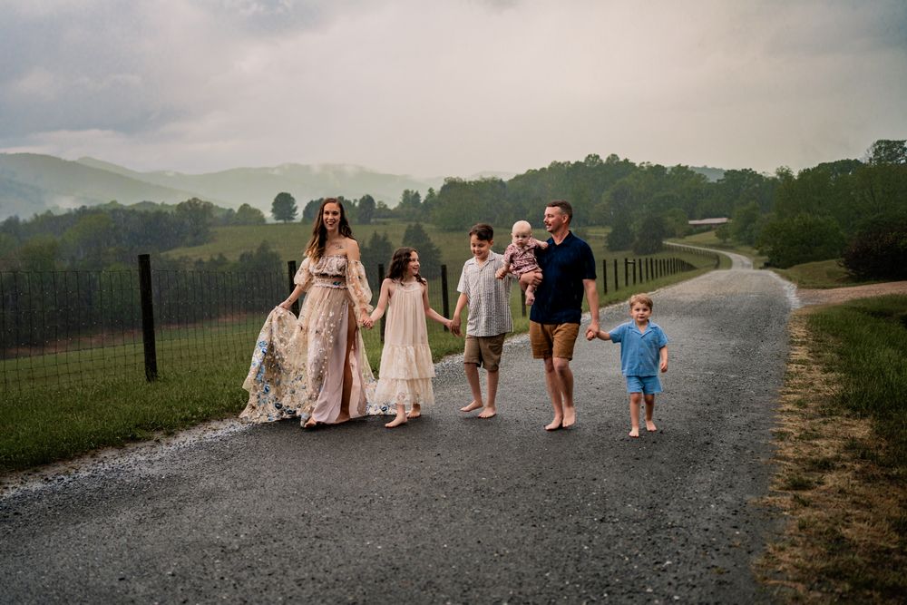 A group of people walking along a misty countryside path wearing formal attire and carrying umbrellas.