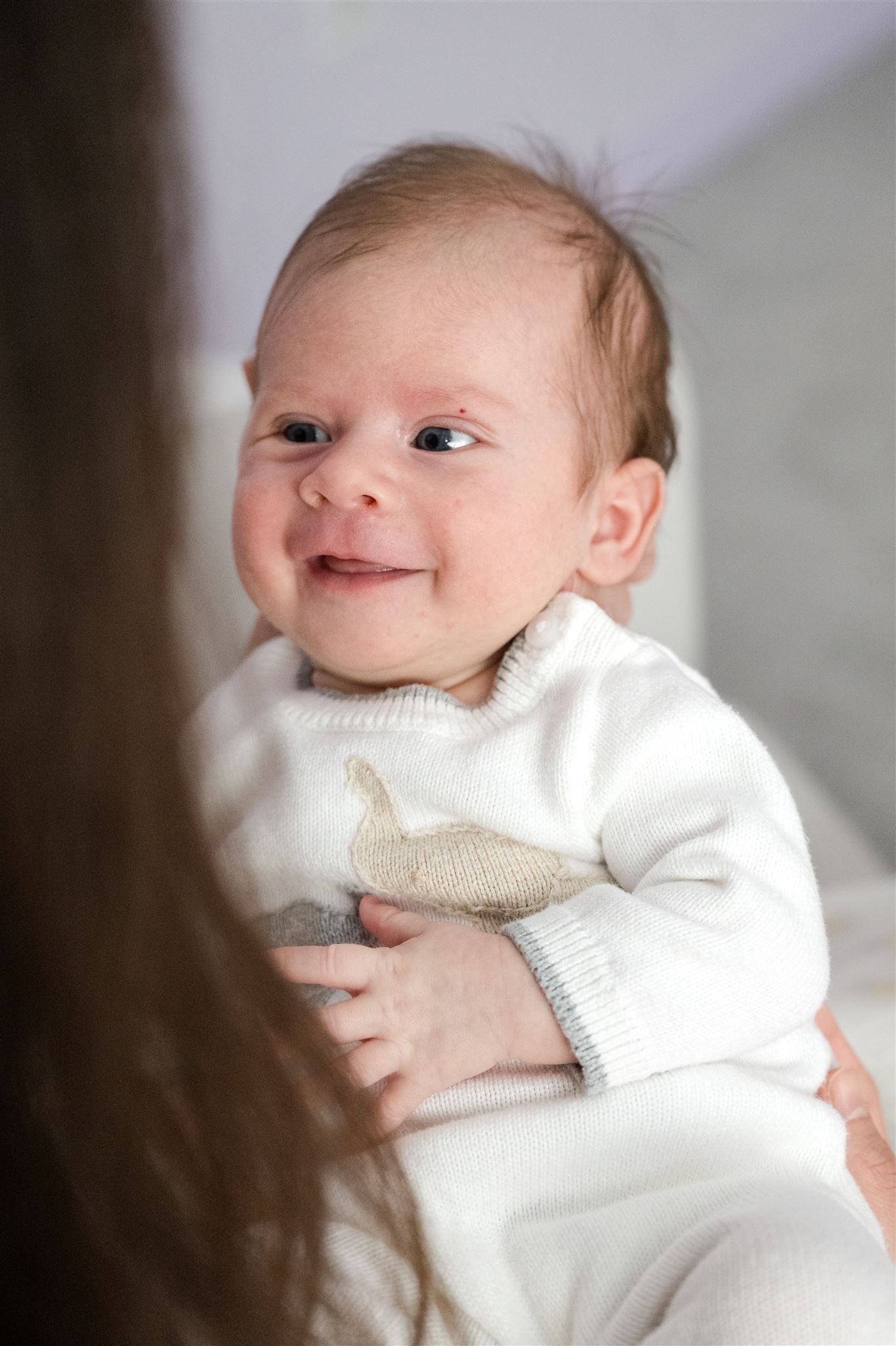 Four heartwarming images of a newborn baby wearing a soft white sweater showing different sweet expressions.